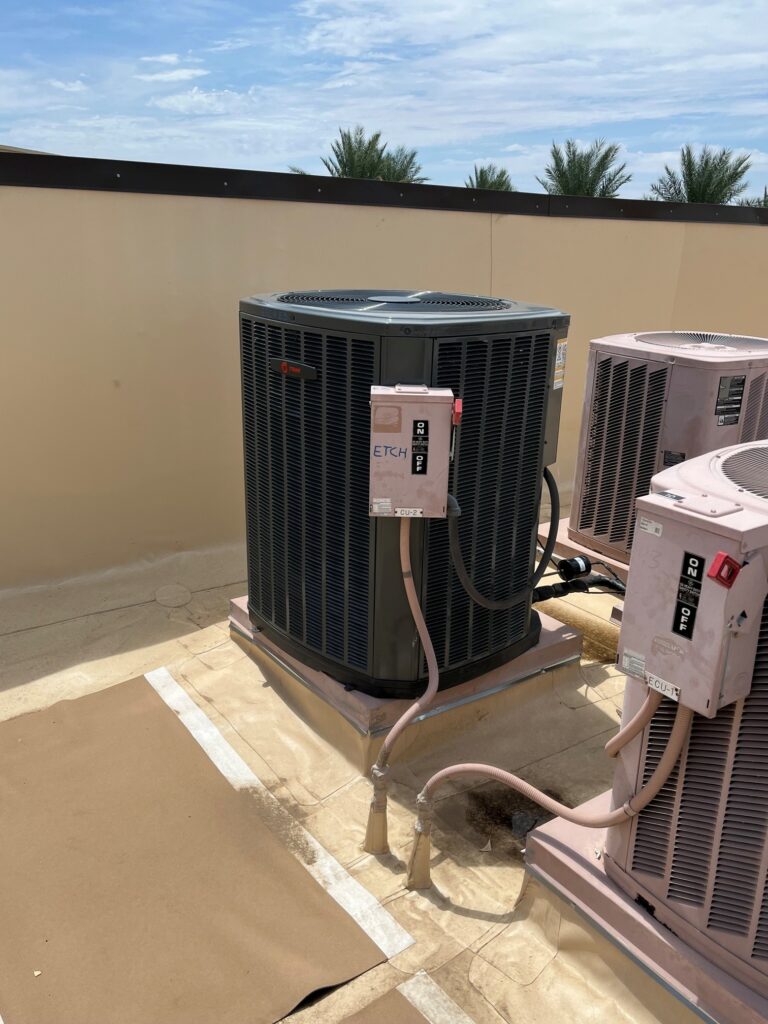 New Trane condenser unit installed on a commercial rooftop next to older units under a blue sky.
