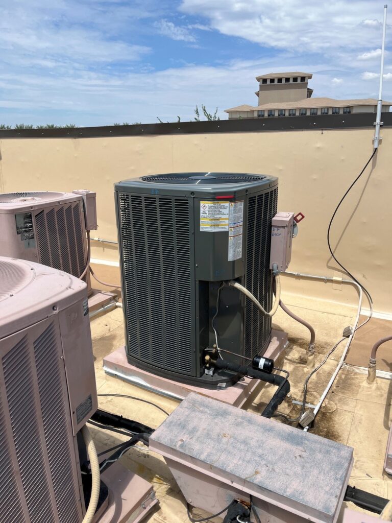 A new Trane split system condenser unit installed on a commercial rooftop, with older units nearby under a blue sky.