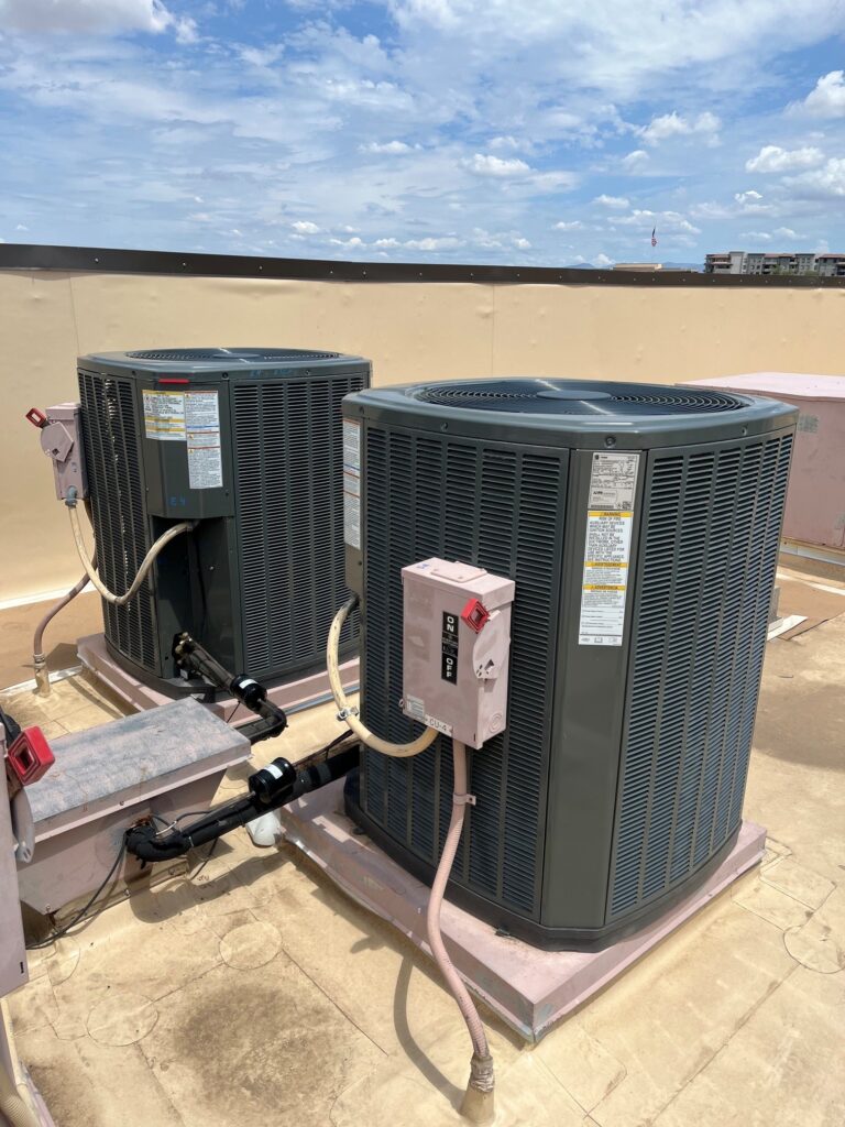 Two new Trane commercial split system outdoor condenser units installed on a flat rooftop under a blue sky.