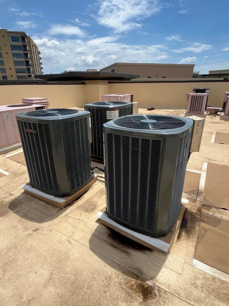 Three new Trane split system air conditioning condensers are installed on a commercial rooftop under a blue sky.