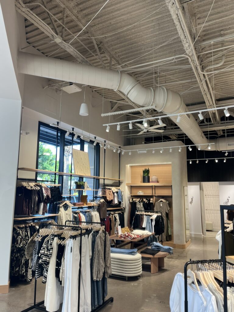 Exposed white spiral ductwork installed in the high ceiling of a modern retail clothing store.