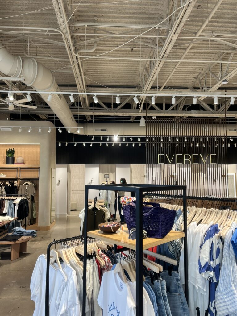 Exposed spiral ductwork in the ceiling of a modern commercial clothing store, with racks of clothes in the foreground.