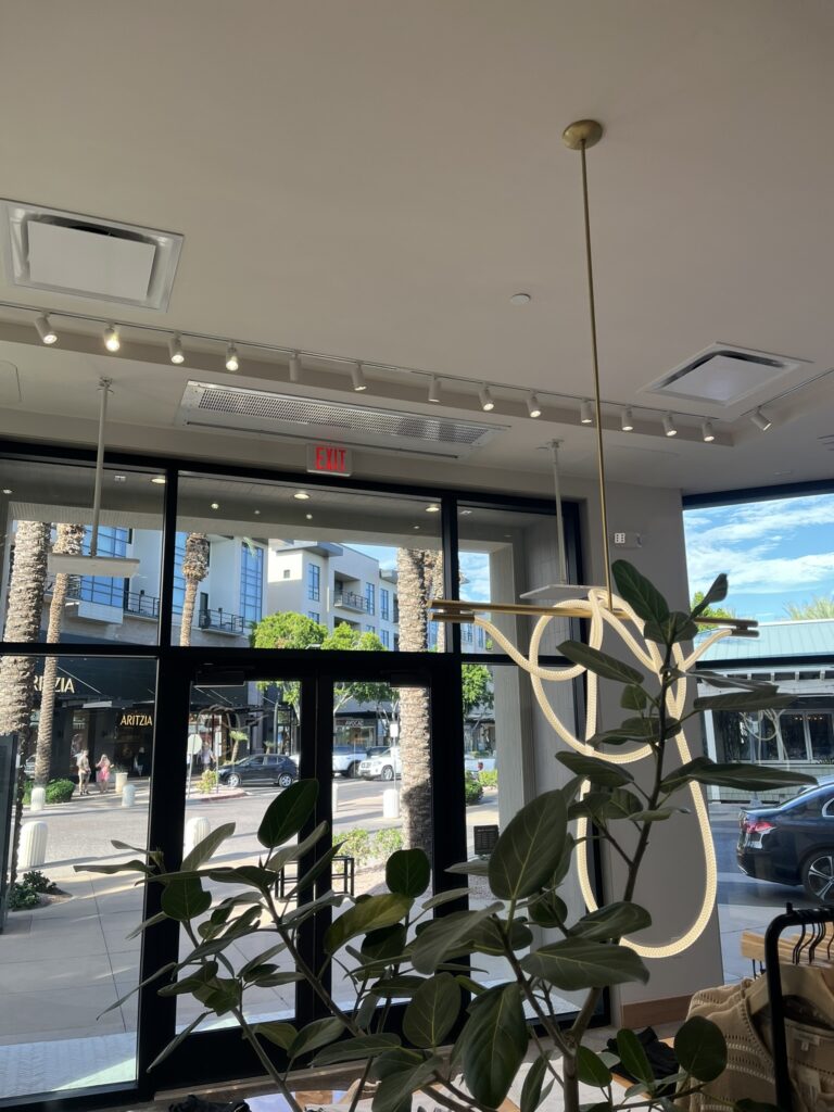 Ceiling-mounted HVAC supply registers and a linear grille in a modern commercial lobby with large windows.