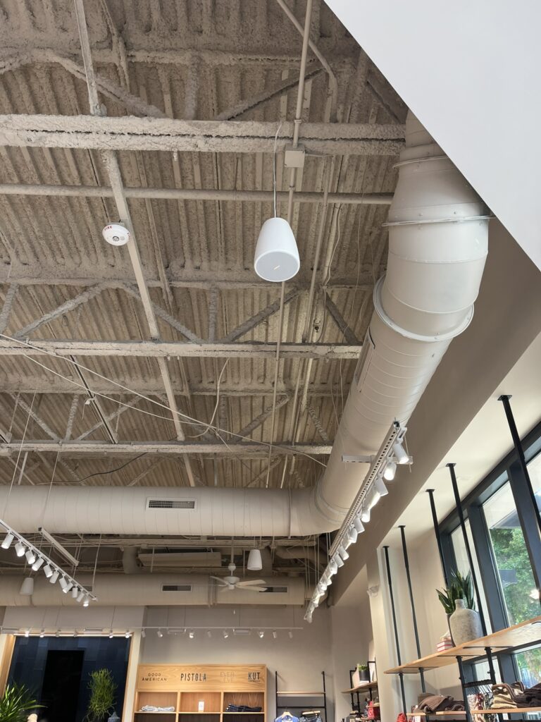 Exposed white spiral ductwork and supply vents visible in the high ceiling of a modern commercial retail store.