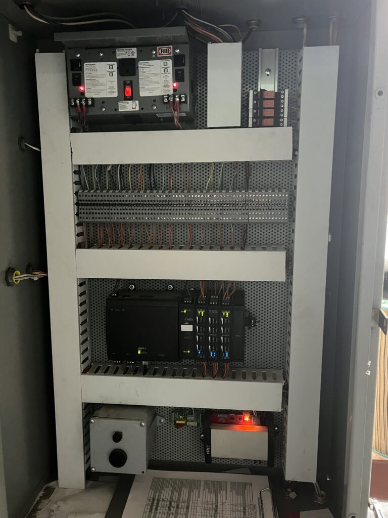 Interior view of an open commercial HVAC control panel with circuit breakers, wiring, and a Delta Controls module.
