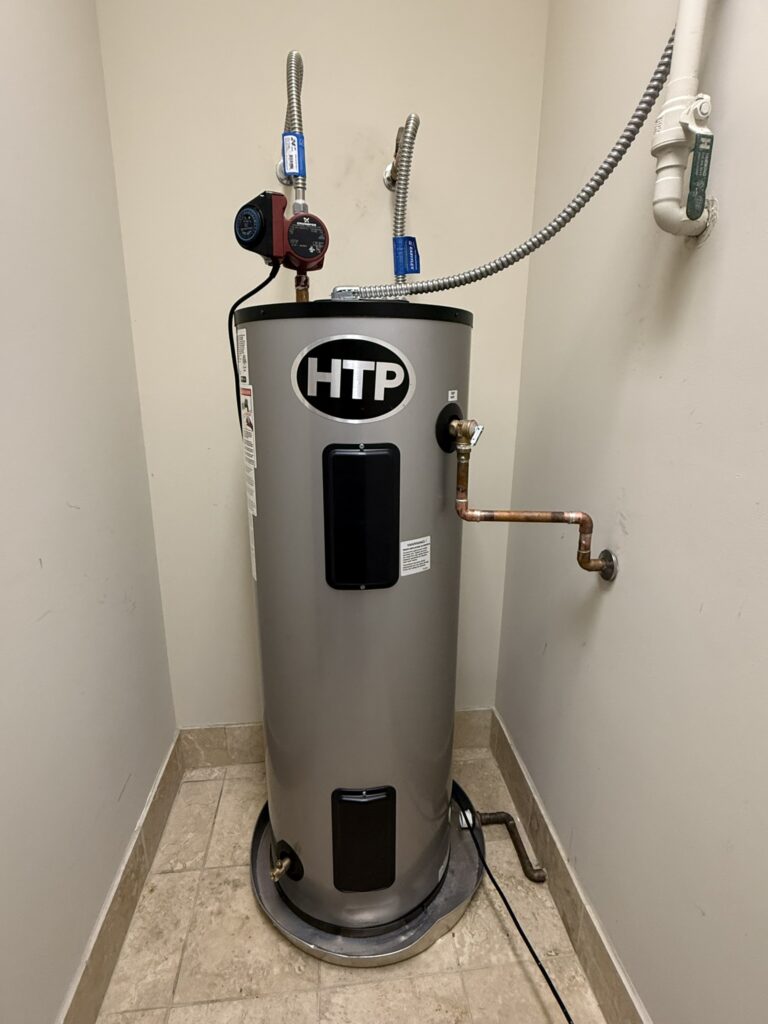 A newly installed HTP 40-gallon stainless steel water heater with a circulator pump in a tiled utility alcove.