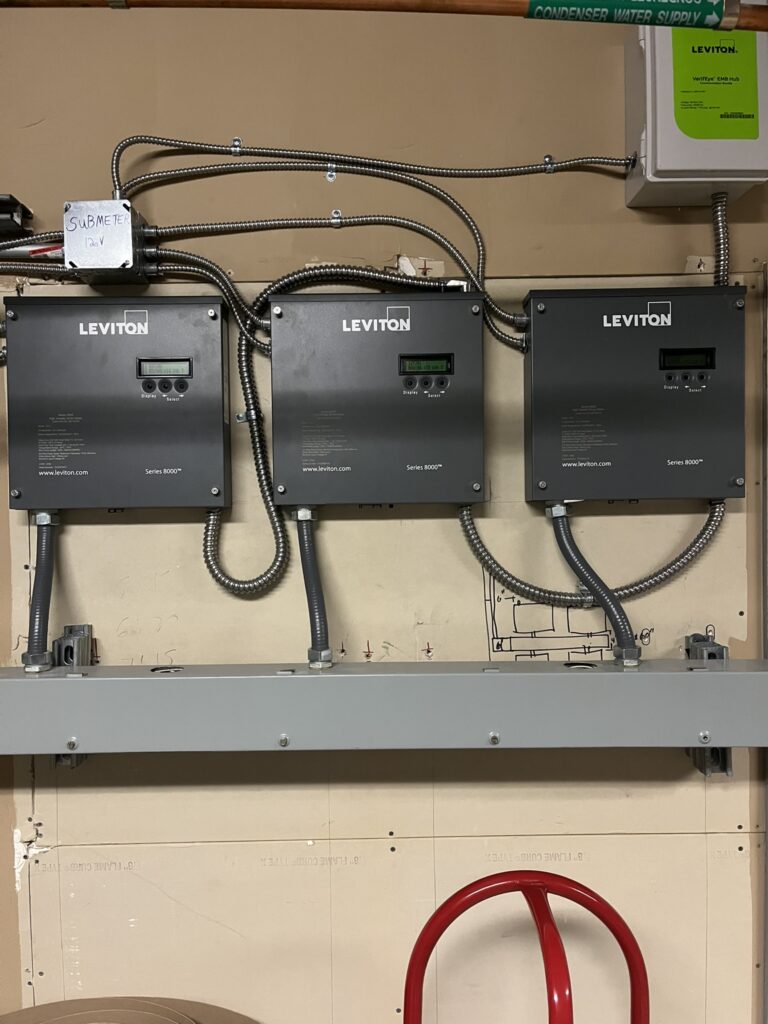 Three Leviton Series 8000 submeter panels and a VerifEye EMB Hub installed on a wall, with a condenser water supply pipe.