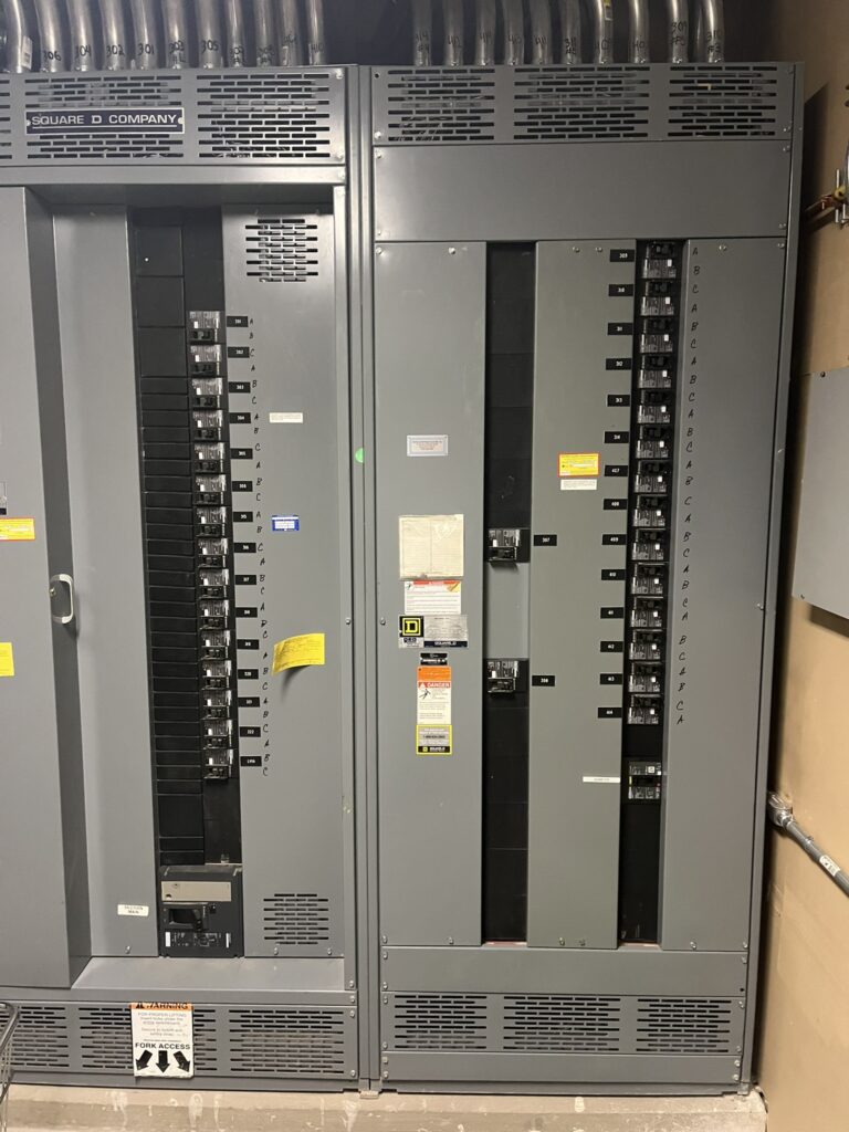 Two large gray Square D electrical submeter panels with numerous circuit breakers and conduits in a commercial building.
