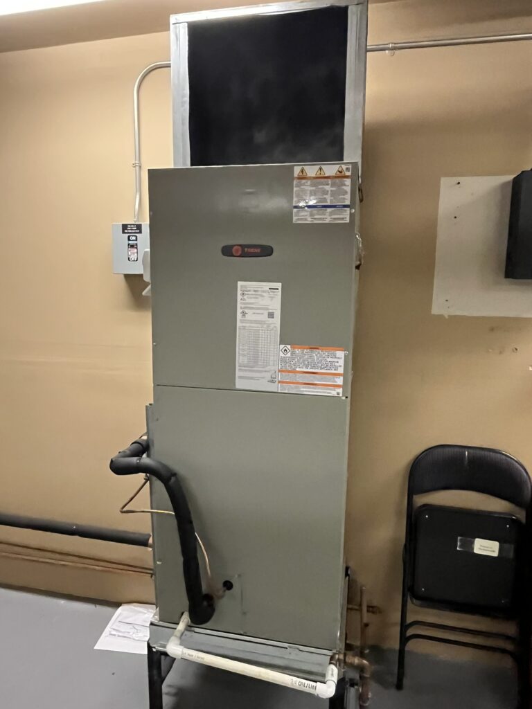 A new Trane air handler unit installed in an interior utility space, with ductwork, refrigerant lines, and a drain line connected.