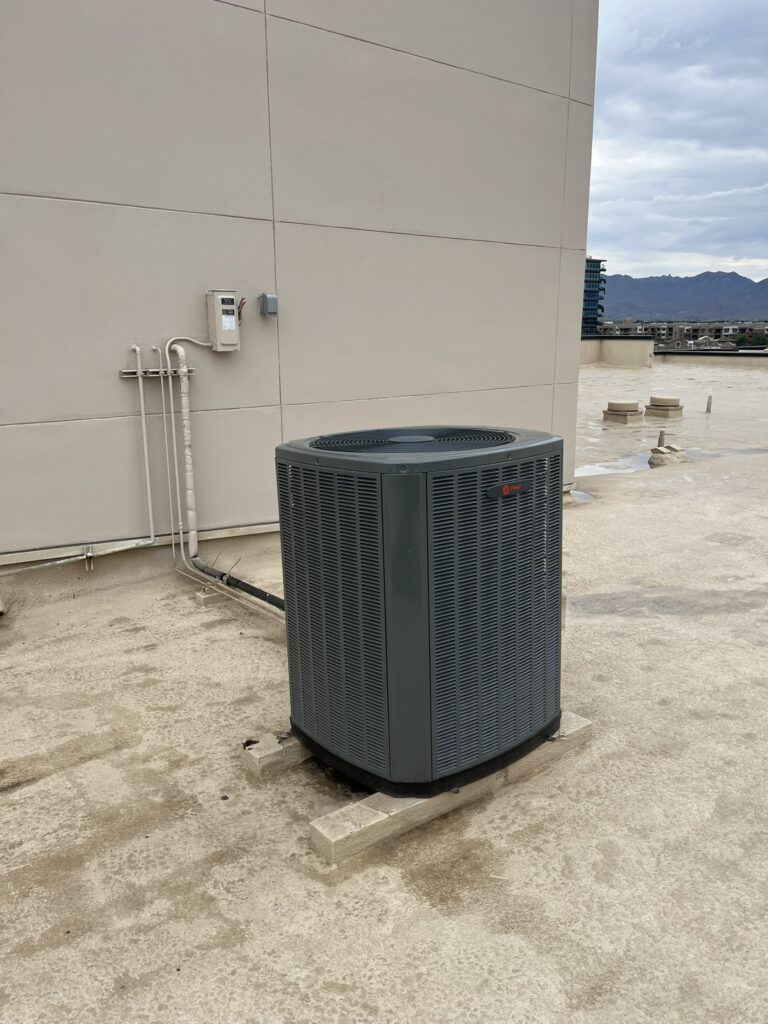New Trane condenser unit installed on a commercial rooftop with conduit connections to the building wall.