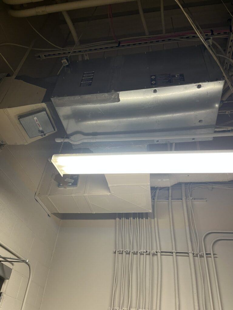 A newly installed ClimateMaster water source heat pump unit suspended from a ceiling, connected to ductwork and electrical conduits.