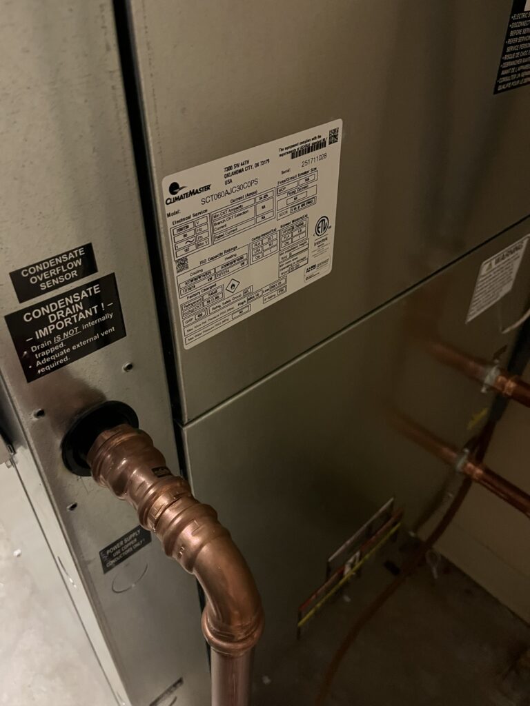 Close-up of a newly installed ClimateMaster water source heat pump unit with its nameplate and copper piping in a commercial electric room.