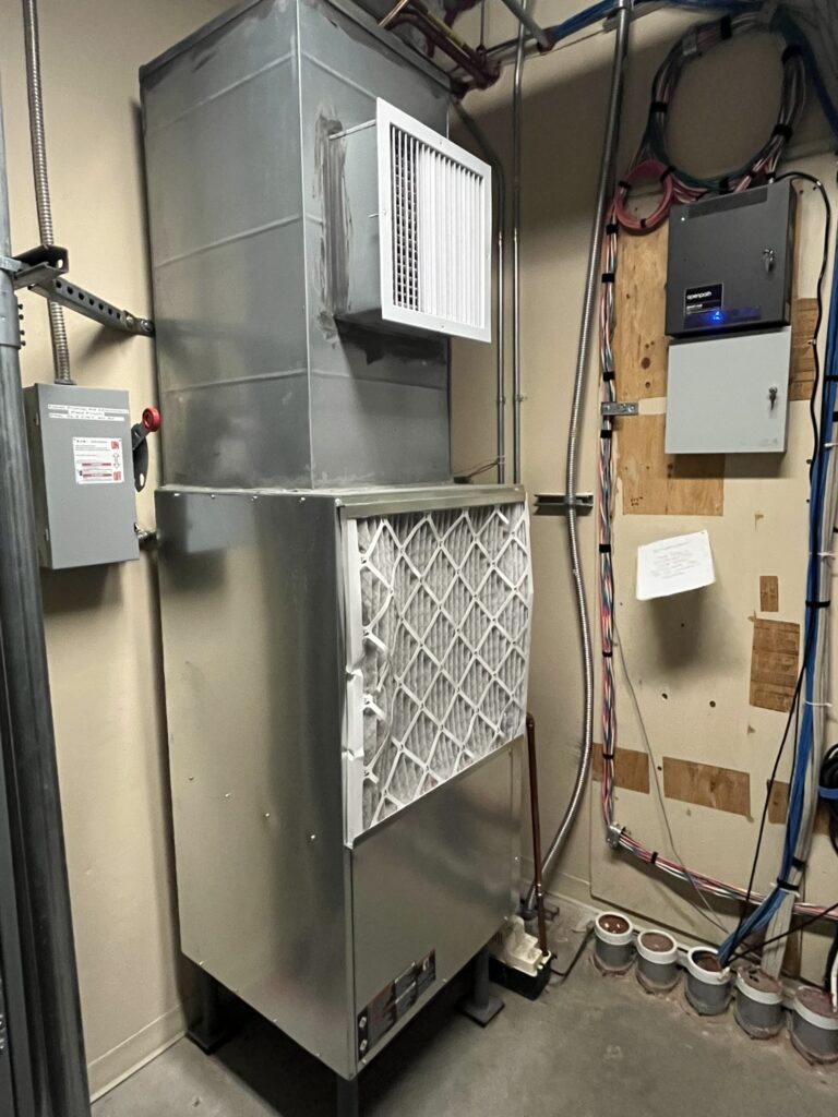 A newly installed Climatemaster water source heat pump unit with attached ductwork and a visible air filter in a mechanical room.