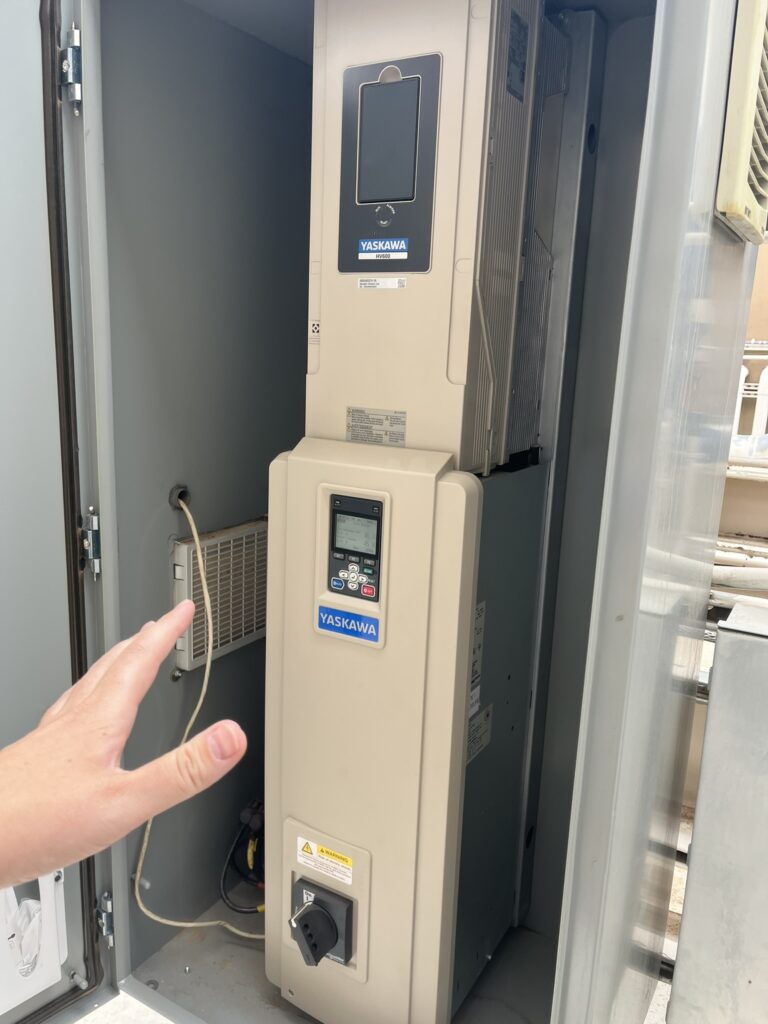 Two large Yaskawa variable frequency drives (VFDs) installed in an open electrical cabinet, with a hand visible.