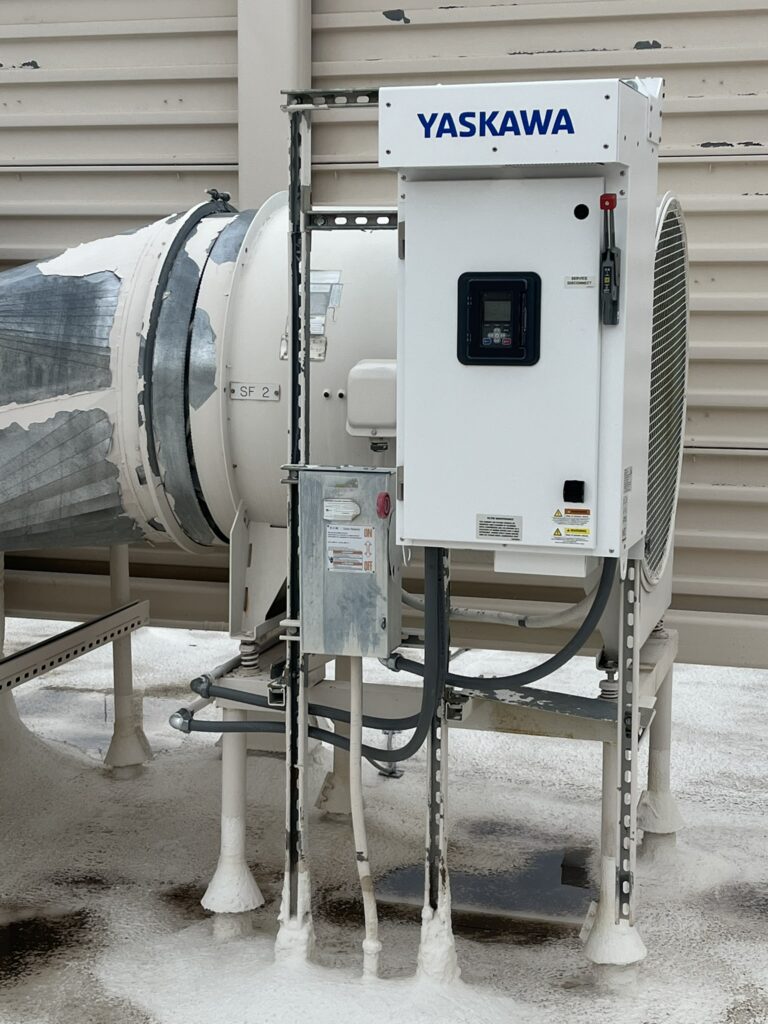 A Yaskawa variable frequency drive control panel installed next to a large supply fan unit on a commercial rooftop.