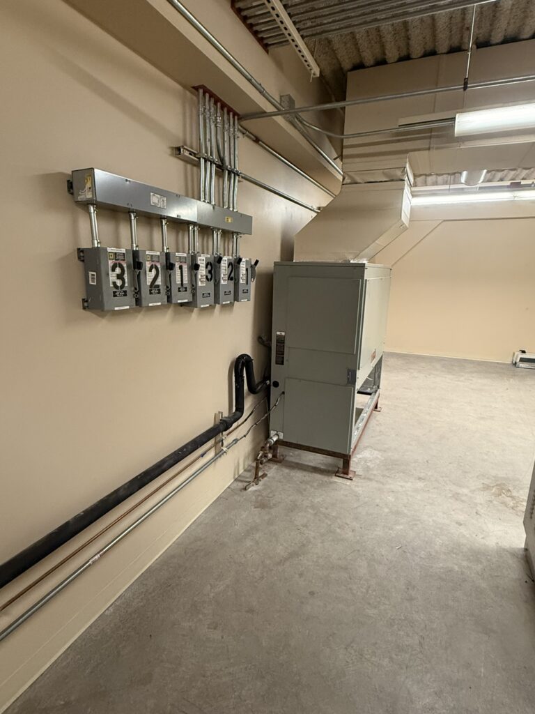 Newly installed gray Trane air handler connected to metal ductwork and electrical conduit in a commercial space.