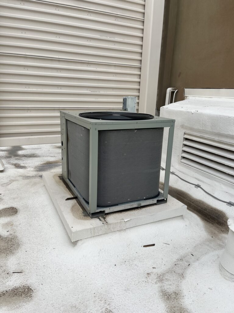 New Trane 10-ton condenser unit installed on a white commercial rooftop next to a roll-down door.