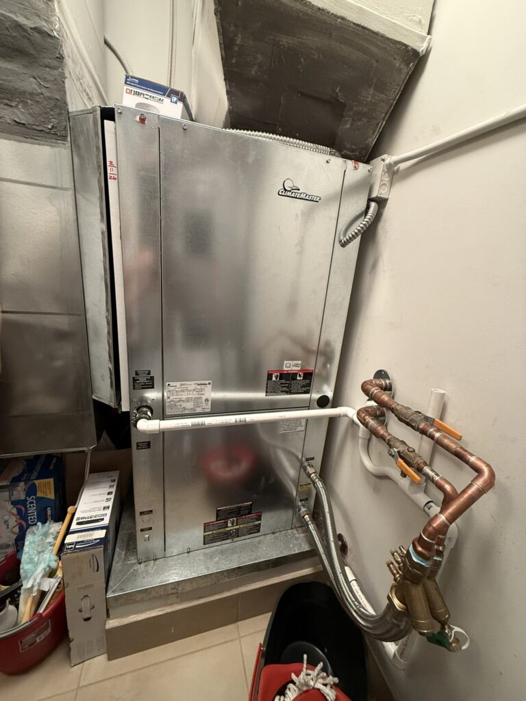 A newly installed ClimateMaster water source heat pump unit with visible piping connections in an indoor utility closet.
