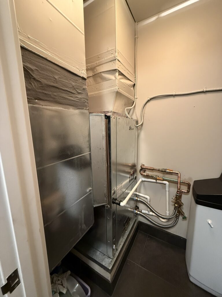 Newly installed indoor water source heat pump unit with ductwork and piping in a utility closet.
