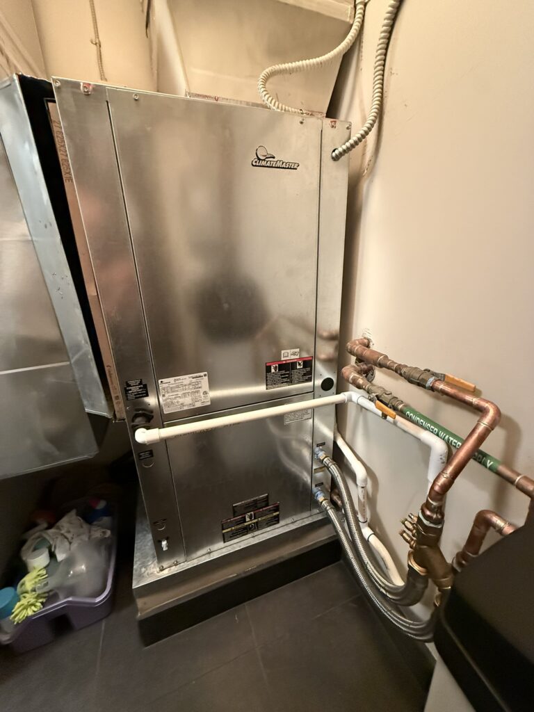 A new Climatemaster water source heat pump unit with connected ductwork and copper and PVC piping in an indoor utility closet.