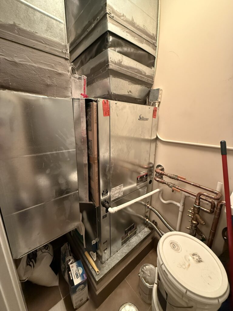 A newly installed ClimateMaster water source heat pump unit with connected metal ductwork and copper piping in an indoor utility closet.