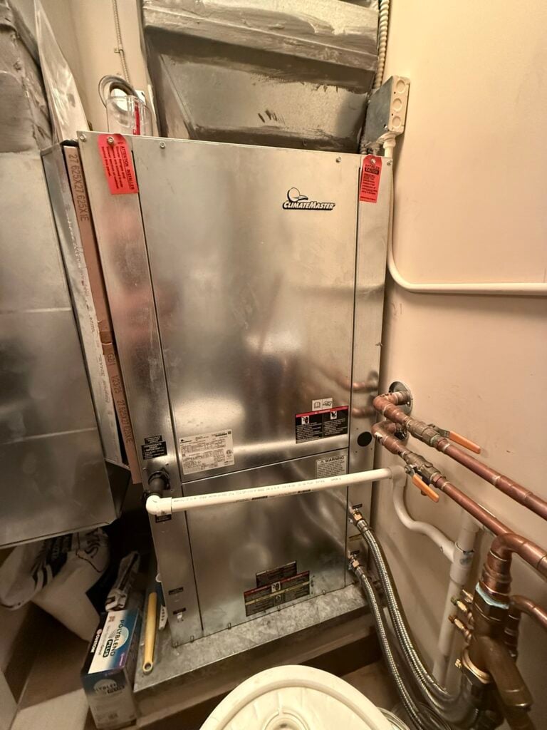 A newly installed ClimateMaster water source heat pump unit connected to ductwork and copper pipes in an indoor utility space.