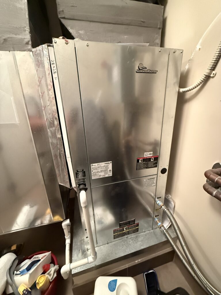 New ClimateMaster water source heat pump unit installed indoors, connected to ductwork and water lines in a utility space.