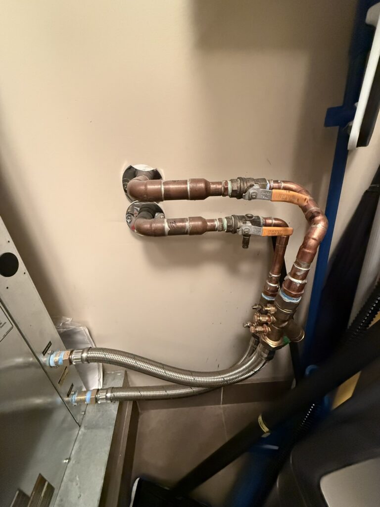 Newly installed copper pipes, valves, and flexible hoses connecting to a water source heat pump unit in an interior space.