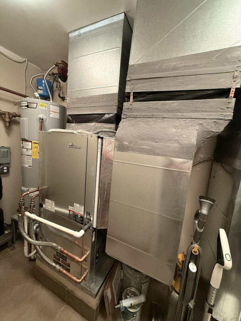 A new ClimateMaster water source heat pump unit installed in a utility closet, connected to metal ductwork and plumbing.