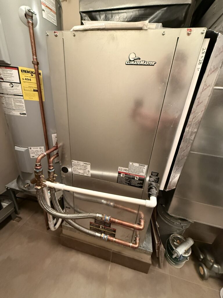 A newly installed ClimateMaster water source heat pump unit with copper piping and ductwork, next to a water heater.