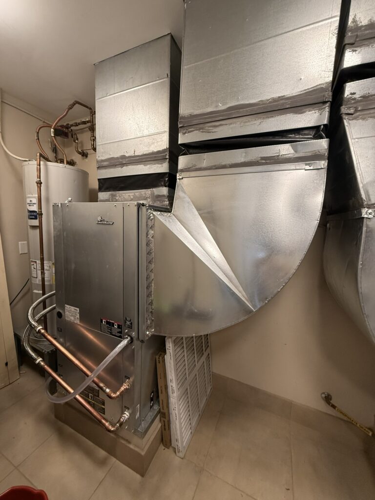 Newly installed ClimateMaster water source heat pump connected to galvanized ductwork in an indoor utility space.