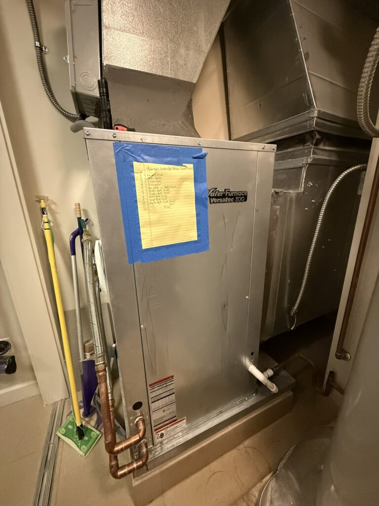 A newly installed WaterFurnace Versatec 300 water source heat pump unit with connected ductwork and copper piping in a utility closet.