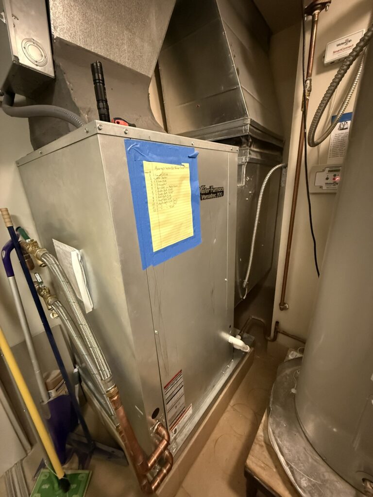 A newly installed silver WaterFurnace water source heat pump connected to ductwork and copper pipes in a utility closet.