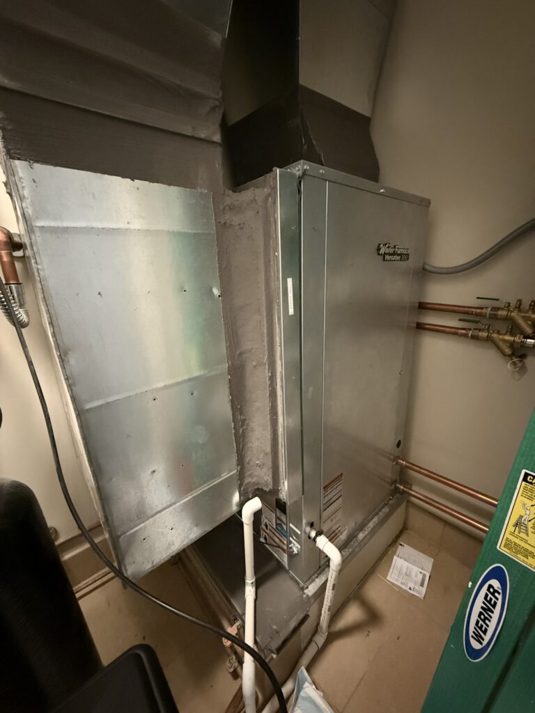 A newly installed WaterFurnace Versatec 300 water-source heat pump unit connected to ductwork and plumbing lines.