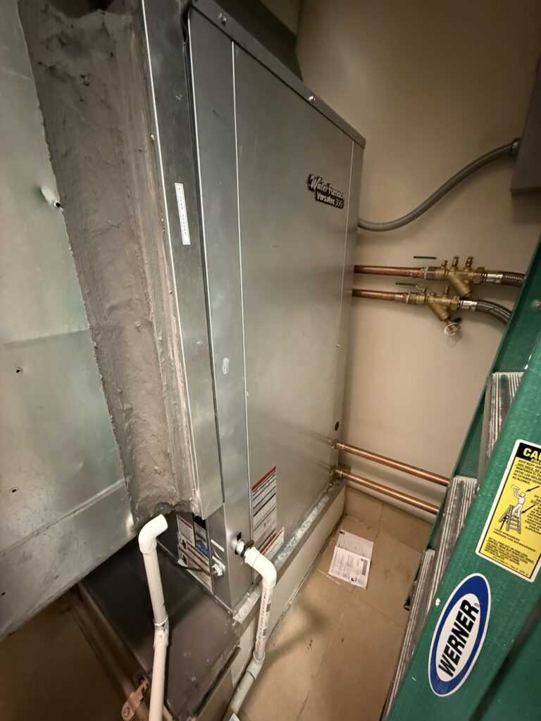 Newly installed WaterFurnace Versatec 300 water source heat pump unit with copper pipes, ductwork, and drain lines.